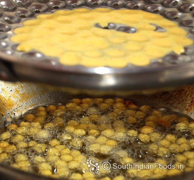 Hold boondi ladle over the pan, pour batter gently shake